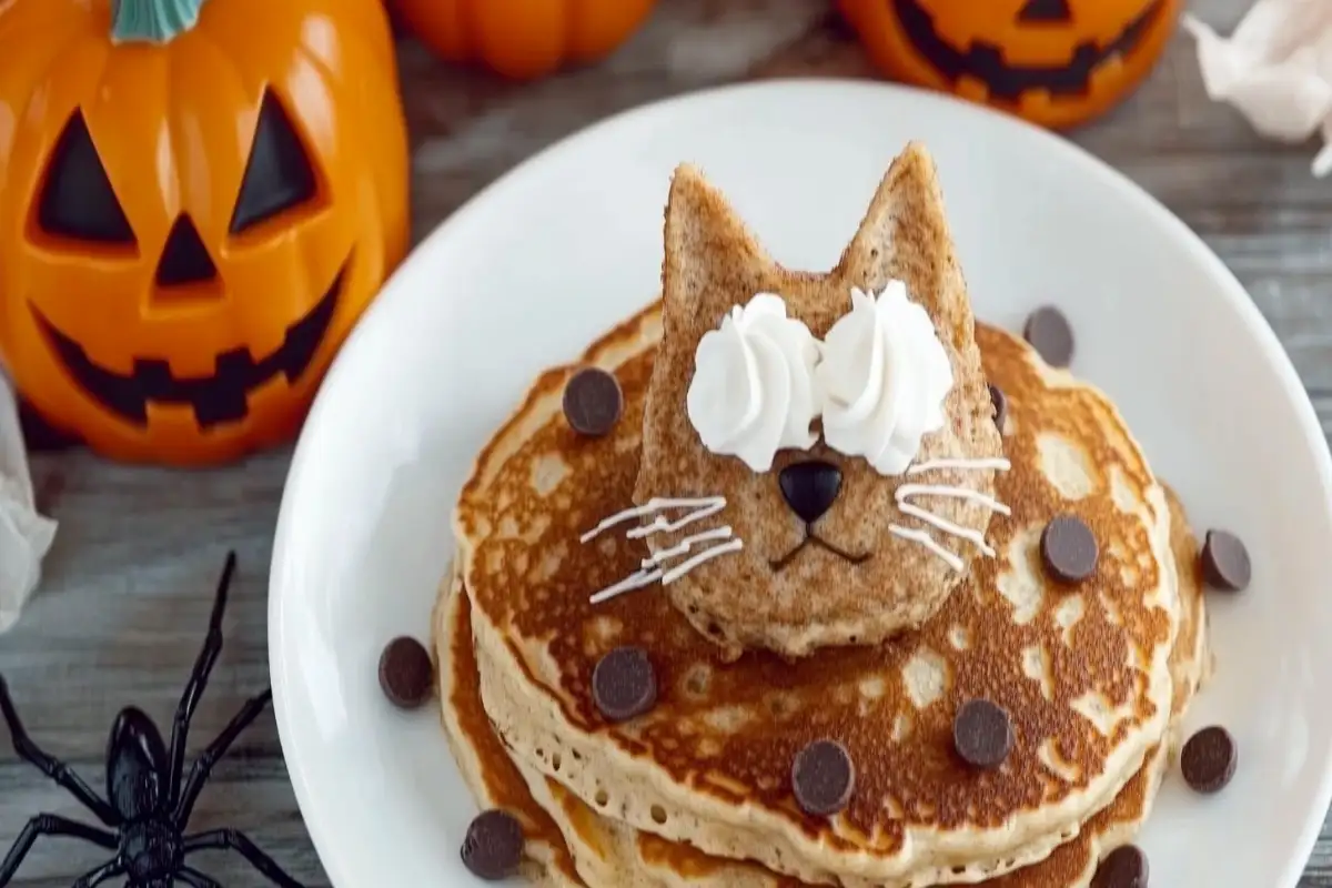 Halloween-themed black cat pancakes with whipped cream whiskers