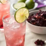 Glass of hibiscus spritz mocktail with ice, lime wedge, and mint garnish