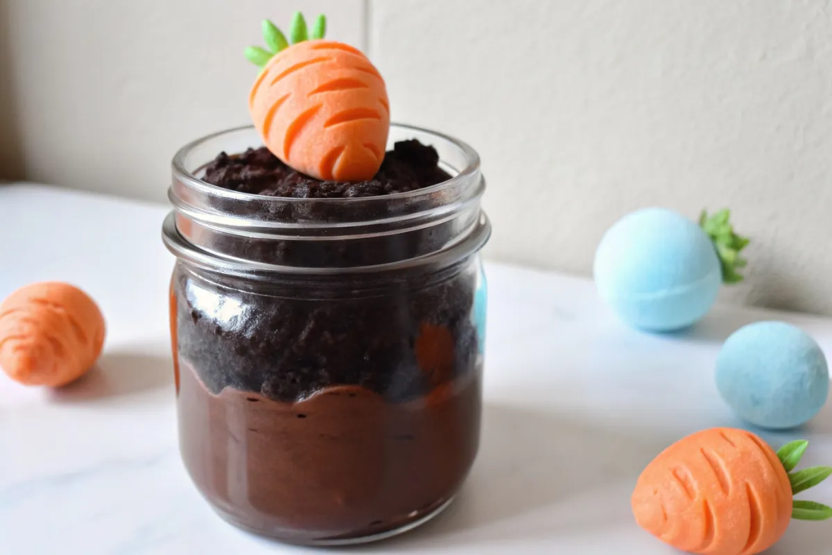 : A festive Dirt Covered Carrot Pudding Cup with layers of chocolate pudding, crushed Oreo dirt, and a chocolate-covered strawberry carrot.