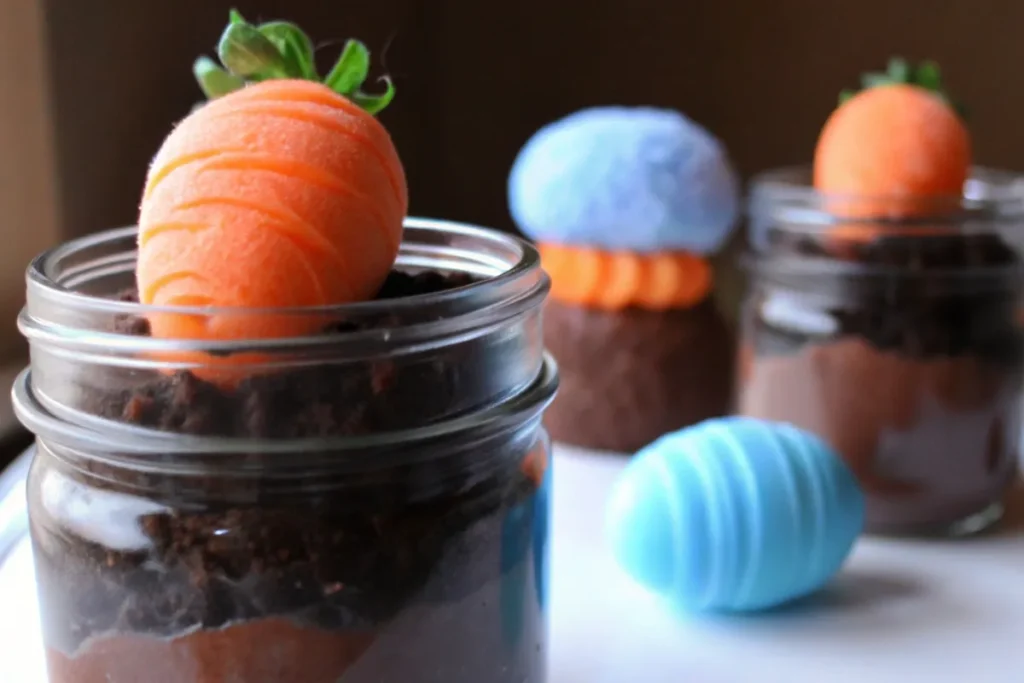 : A festive Dirt Covered Carrot Pudding Cup with layers of chocolate pudding, crushed Oreo dirt, and a chocolate-covered strawberry carrot.