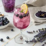 Blueberry lavender mocktail in a wine glass with ice, lavender garnish, and lemon twist – refreshing, alcohol-free floral drink.