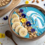 High protein blue vanilla smoothie bowl with banana, granola, and nuts in wooden bowl