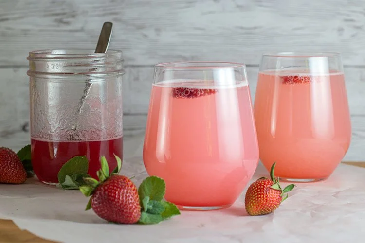 Strawberry rhubarb spritzer in a glass with fresh strawberries and rhubarb.